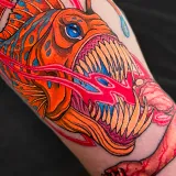 Neo-traditional forearm tattoo of a red anglerfish with sharp teeth, a severed human arm held before its mouth and a streak of blood through the water, designed by Jesse Dee at House of Wolves Tattoo, Geelong